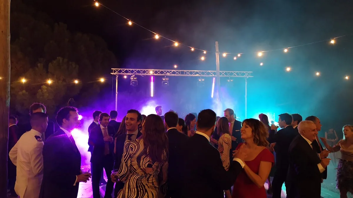 Público bailando bajo iluminación de colores y guirnaldas de luces en un evento nocturno