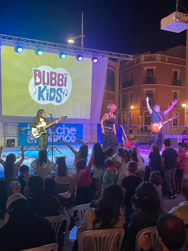 Concierto infantil al aire libre con pantalla, músicos y niños frente al escenario