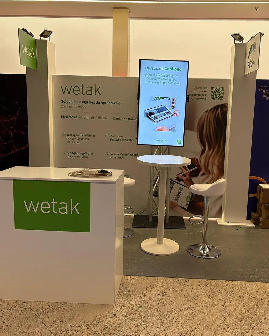 Stand de exposición con pantalla vertical, mostrador y mesa alta en un congreso
