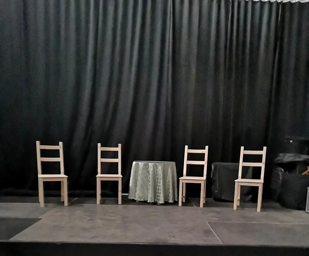 Escenario con telón negro, sillas y mesa preparados para una actuación