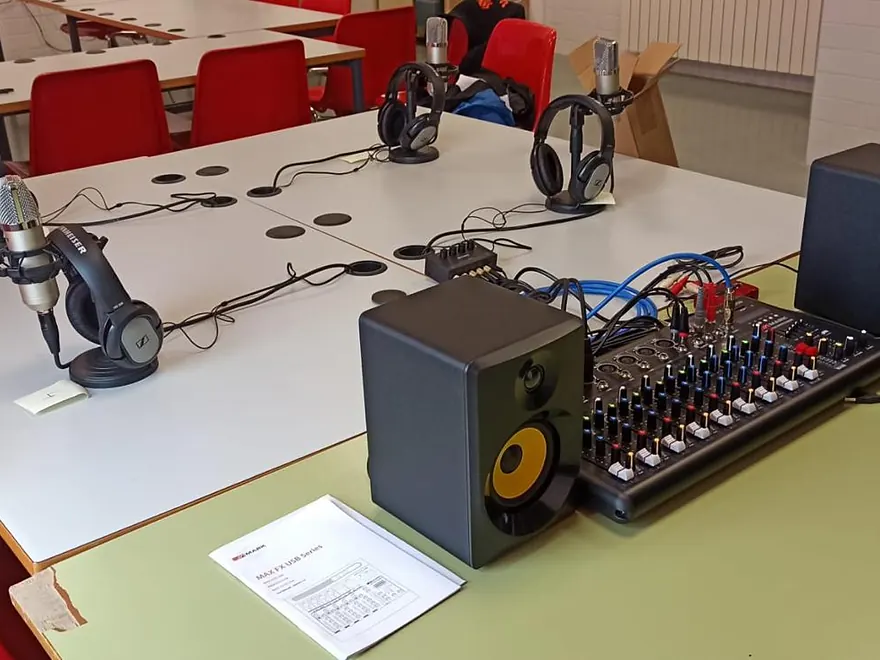 Estudio de radio escolar con micrófonos, auriculares, mesa de mezclas y monitores sobre una mesa de aula